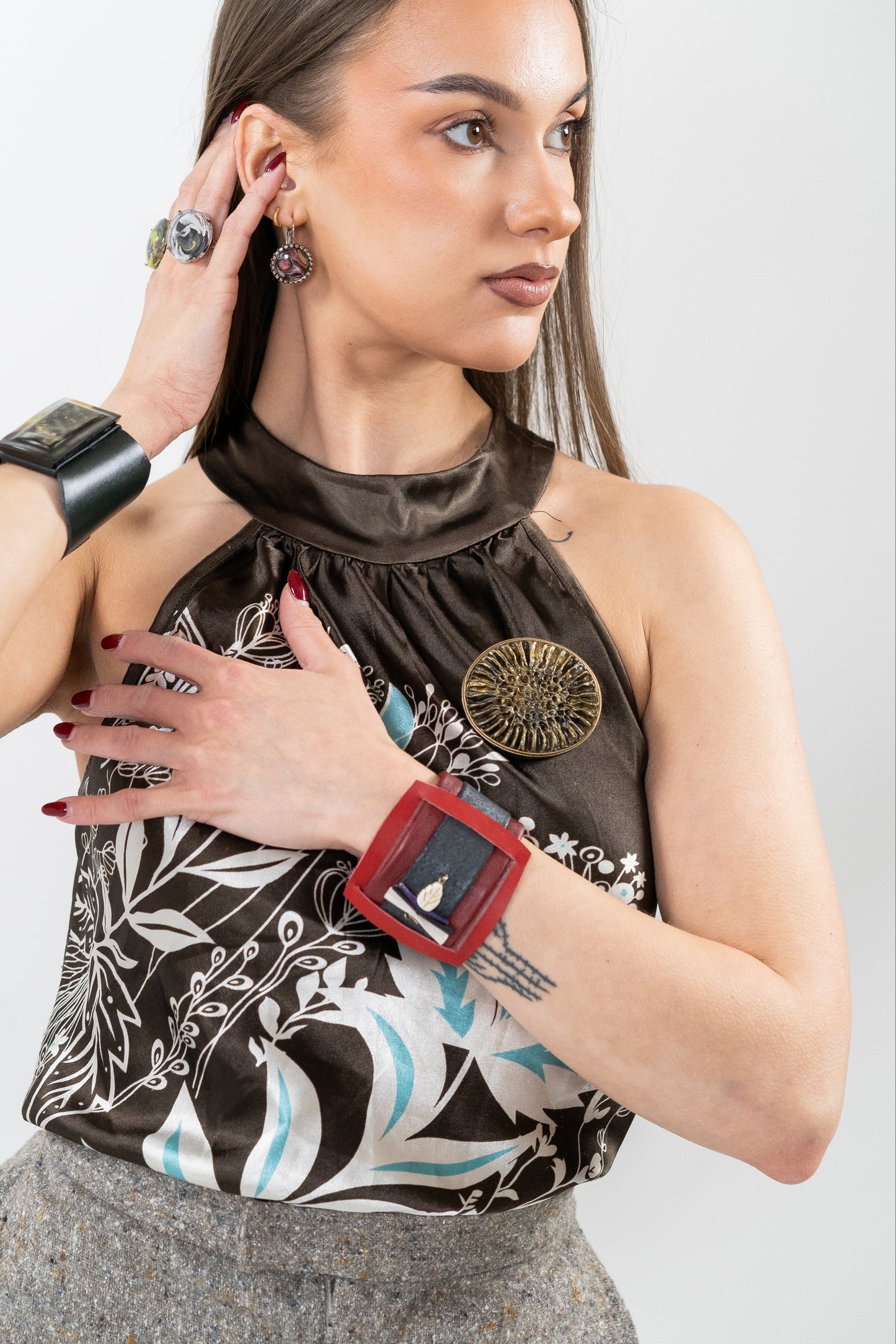 Woman wearing a patterned top with a decorative brooch, gray pants, and a red wristband on a white background