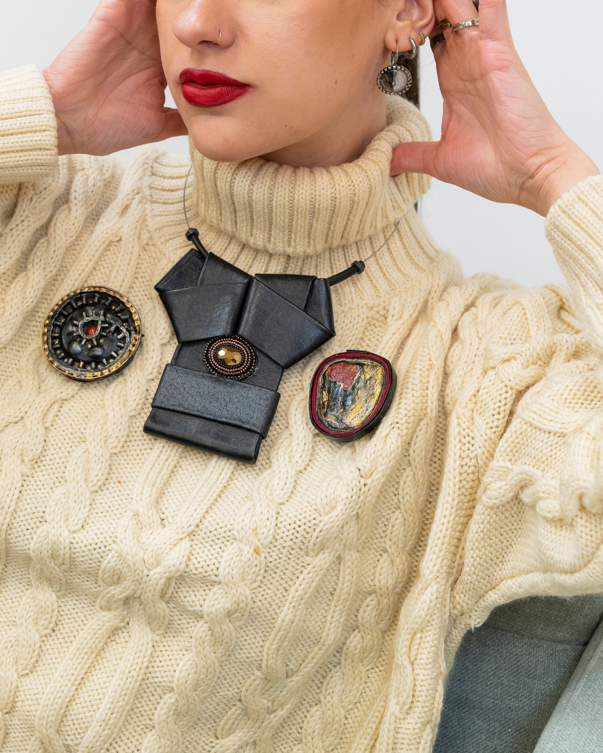 Woman wearing a cream sweater with decorative brooches, posing against a light background.