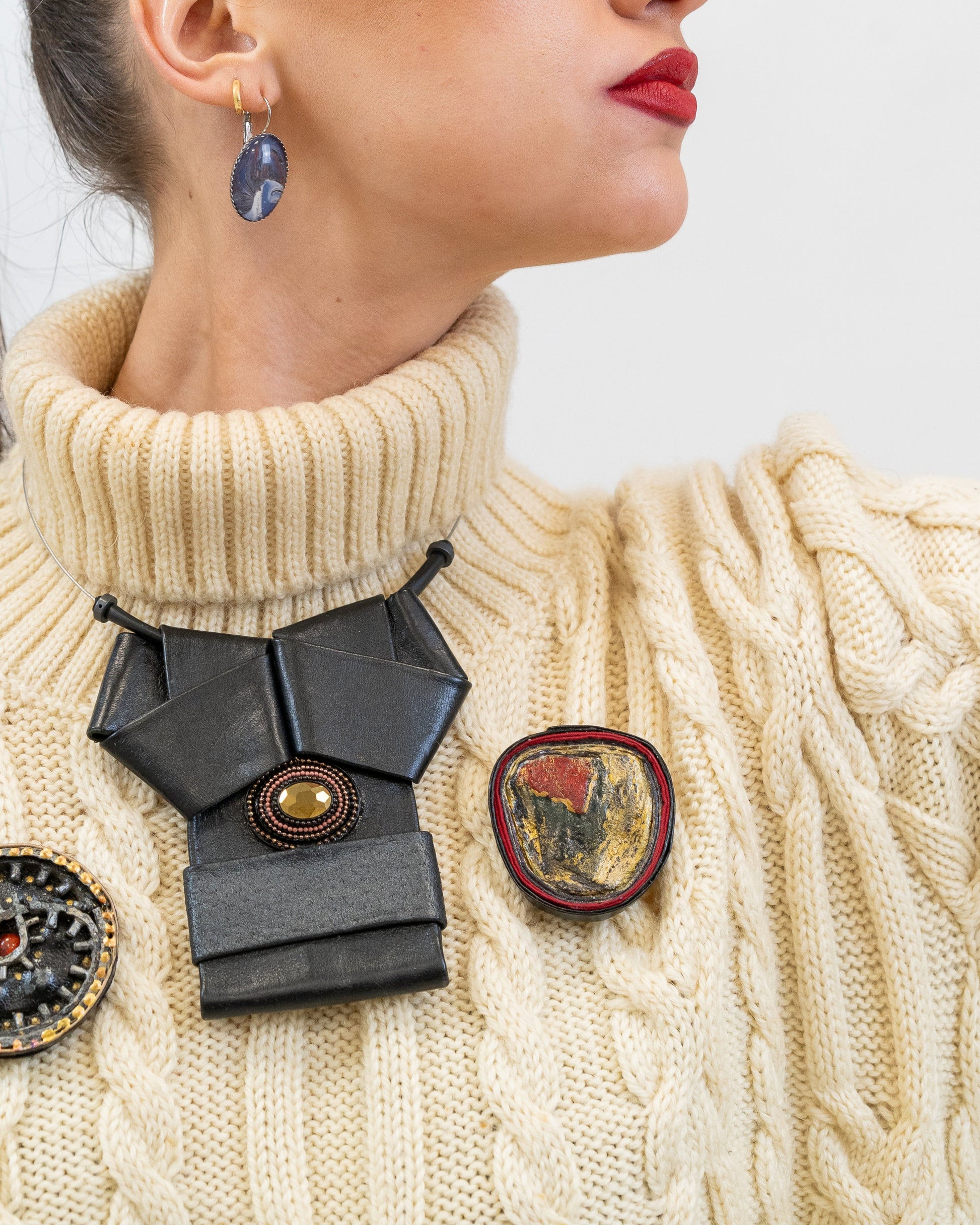 Woman wearing a cream sweater with decorative brooches on a plain background