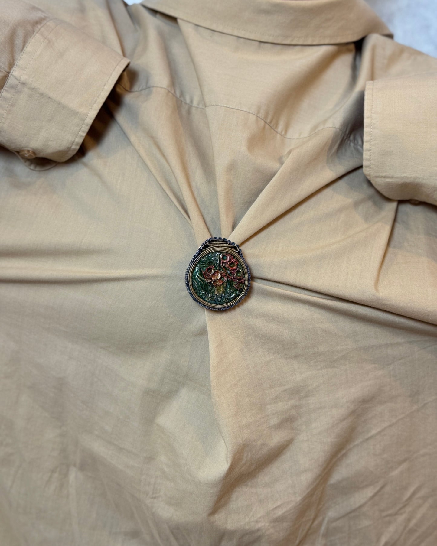 Close-up of a beige shirt with a decorative button on a plain background