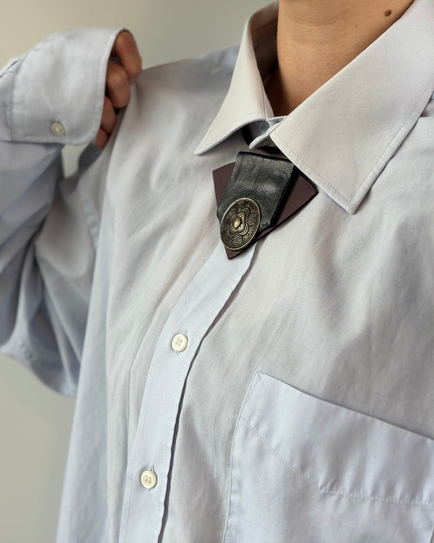 Light blue shirt with a dark tie featuring a decorative button against a neutral background