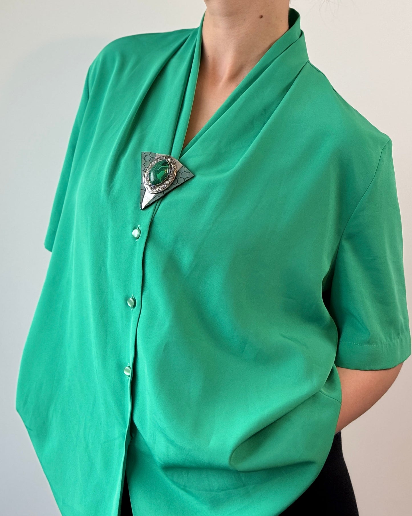 Person wearing a green blouse with a brooch against a plain background