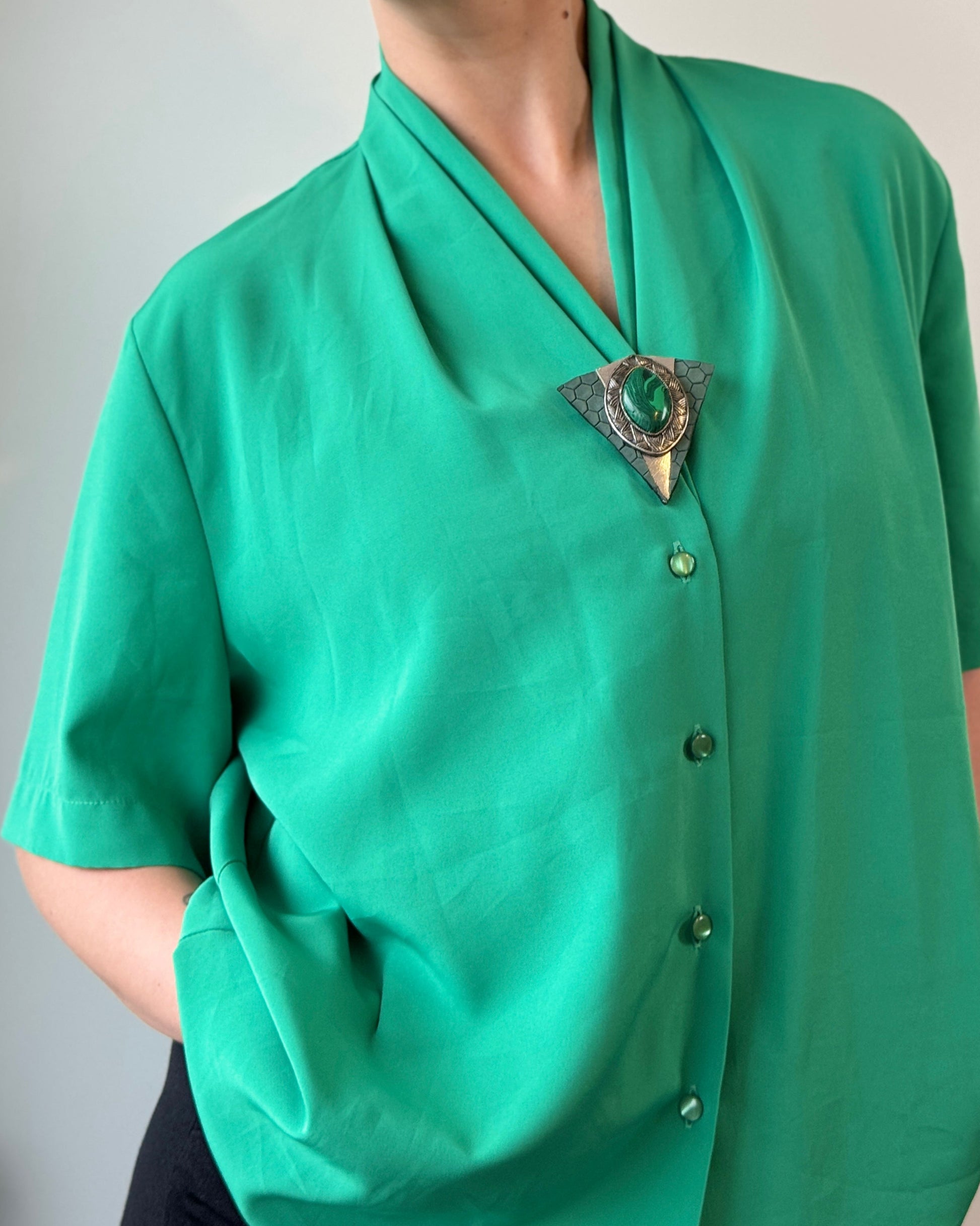 Person wearing a green blouse with a brooch against a plain background