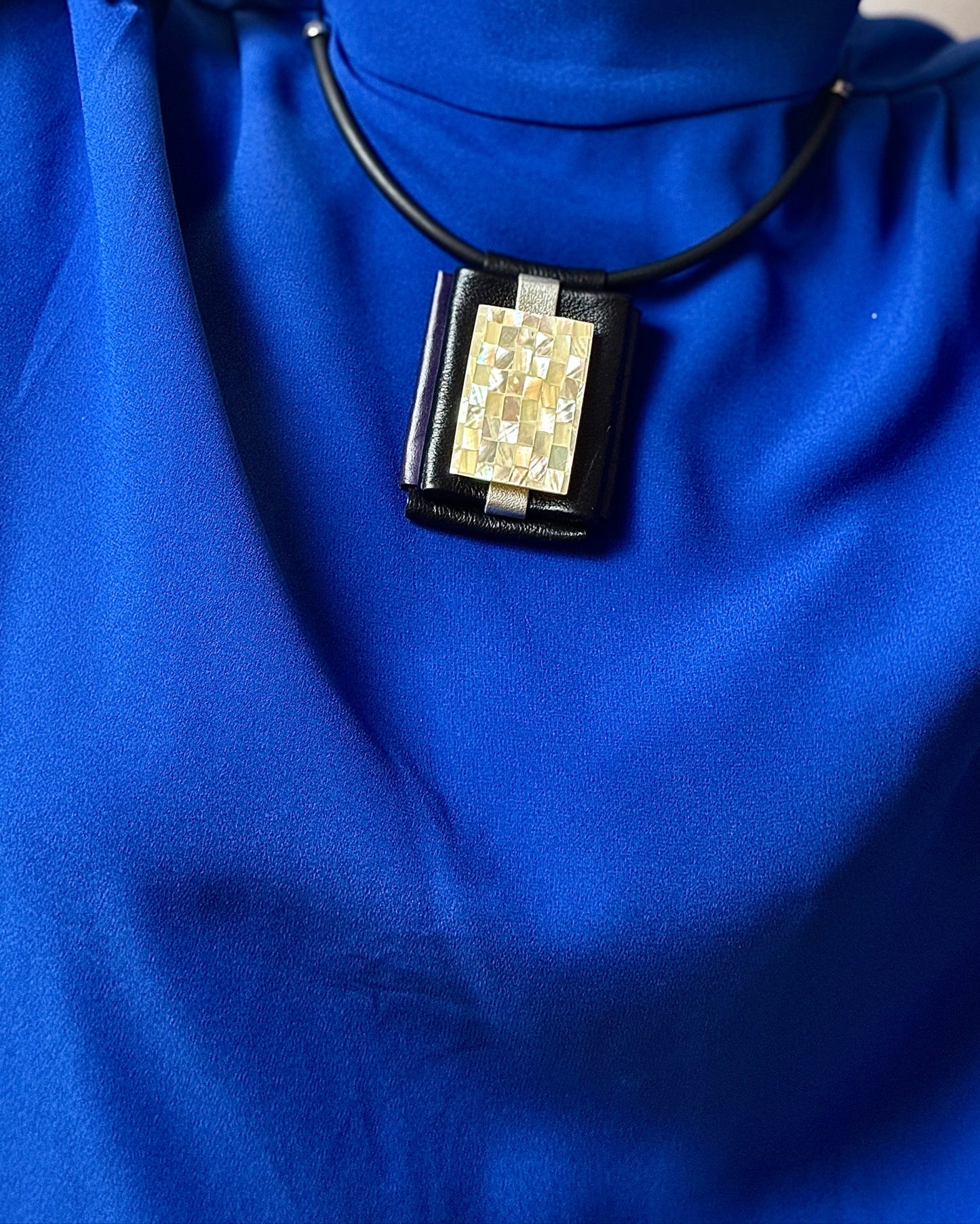Person wearing a blue outfit with a necklace featuring a geometric pendant.