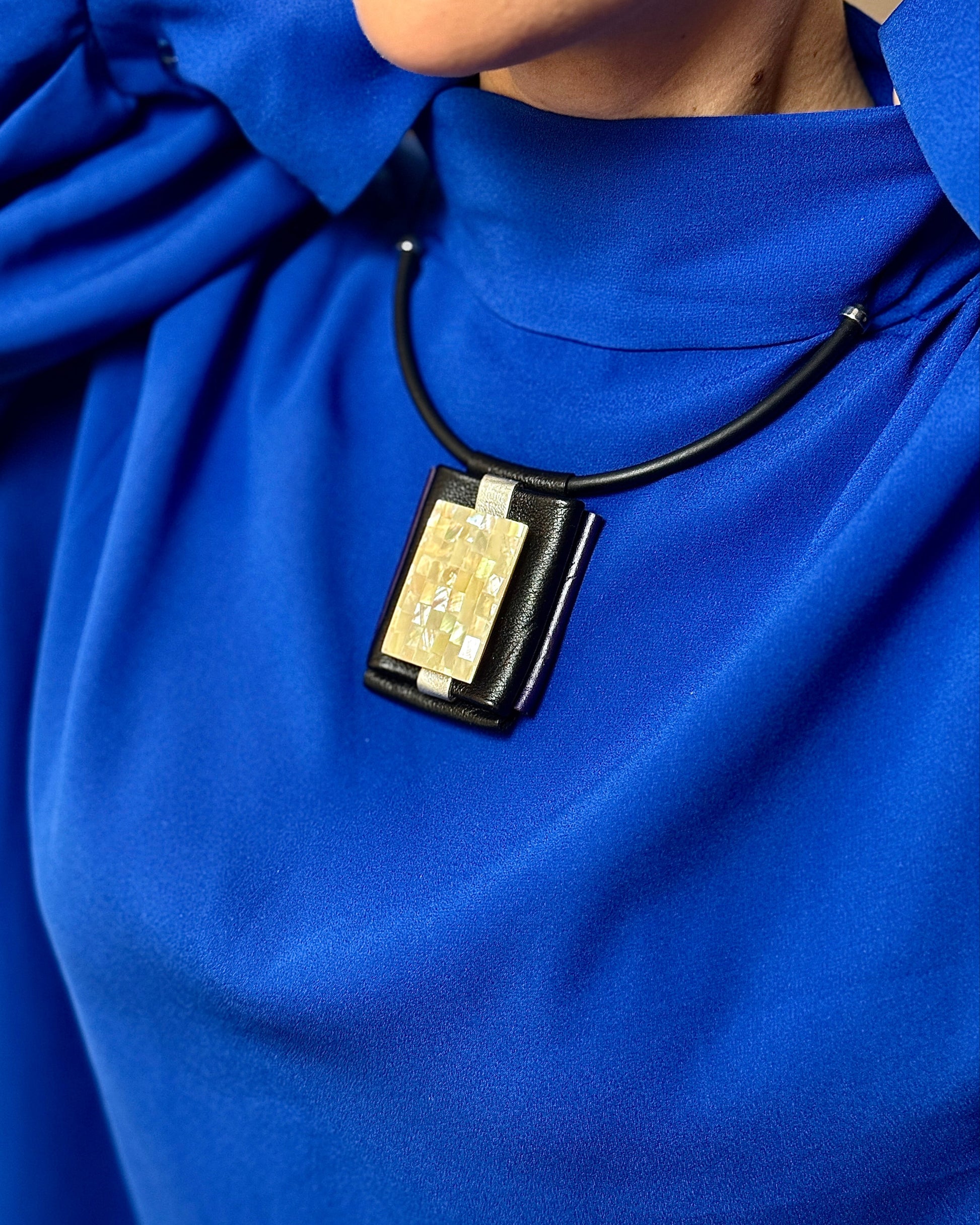 Close-up of a person wearing a blue garment with a necklace featuring a rectangular pendant.