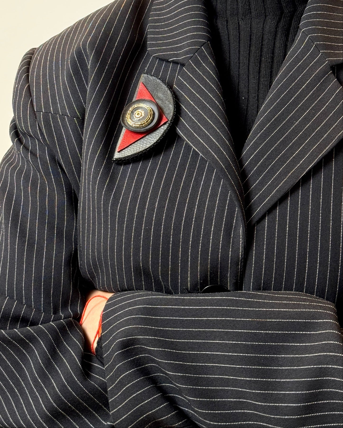 Person wearing a pinstripe coat with a brooch on a neutral background