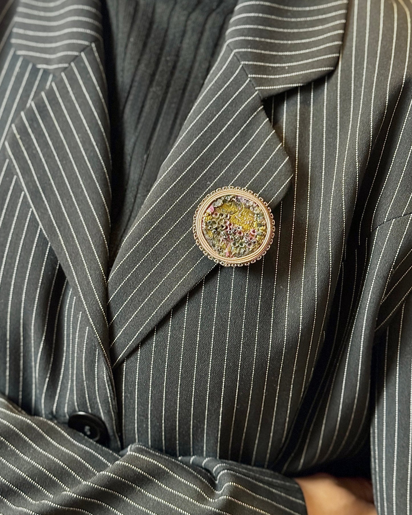 Person wearing a gray pinstripe suit with a decorative brooch on a blurred background