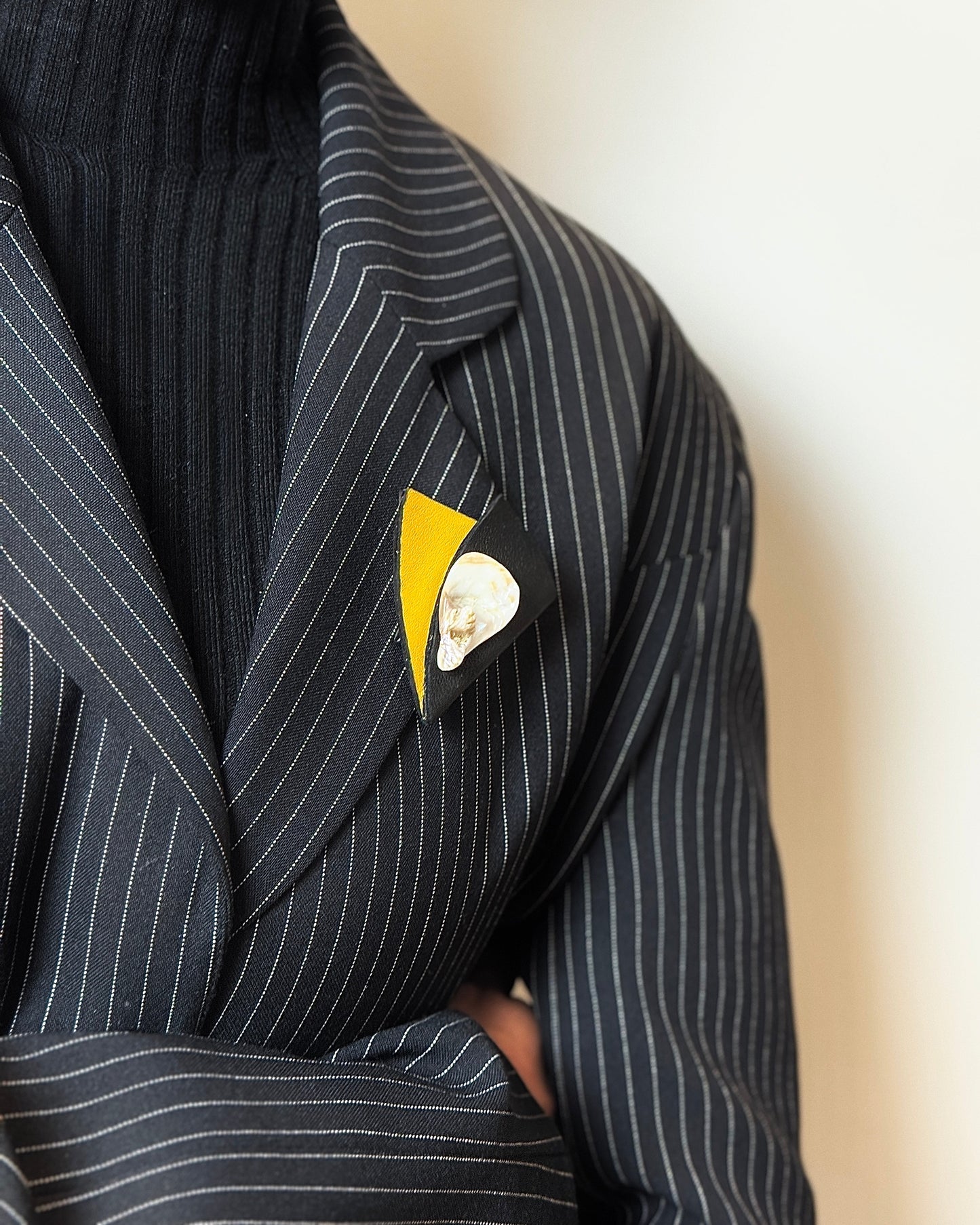 Person wearing a black pinstripe suit with a yellow and white lapel pin on a neutral background