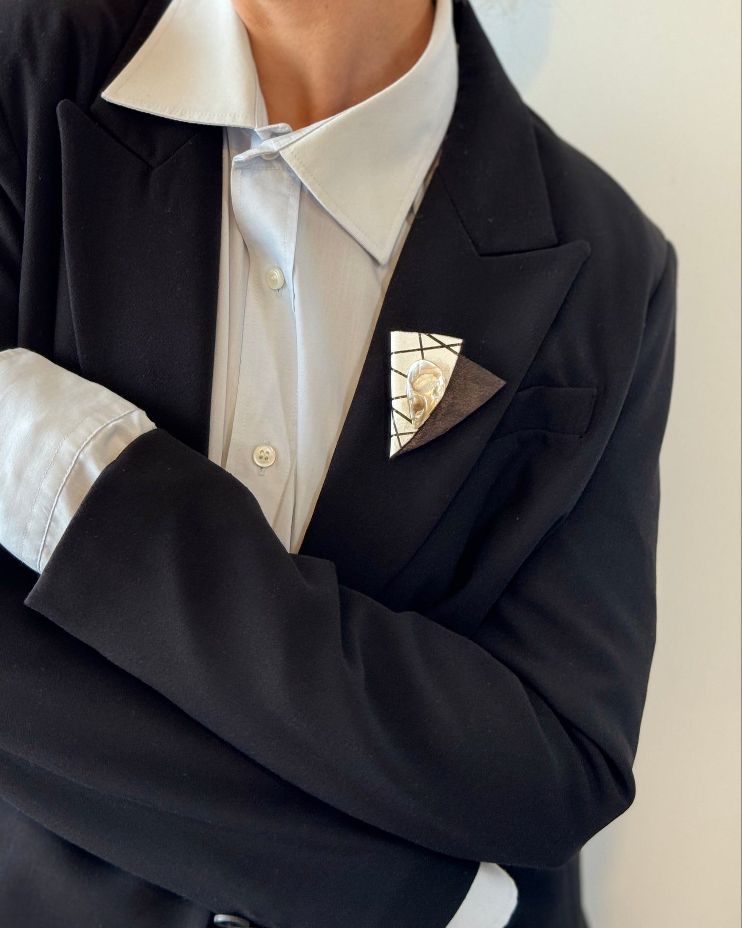 Person wearing a black blazer over a white shirt with a patterned pocket square on a plain background