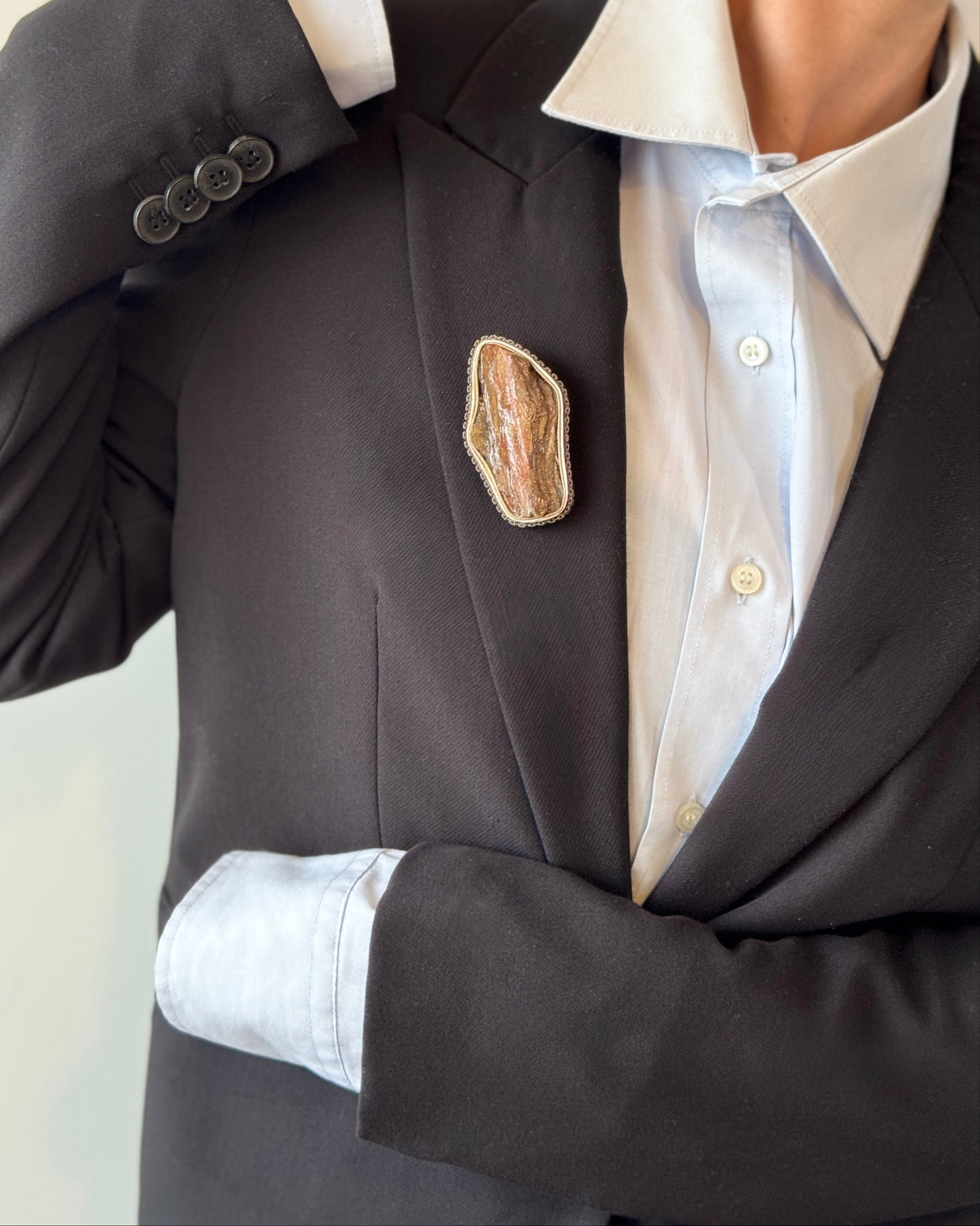 Person wearing a black blazer with a decorative brooch on a plain background