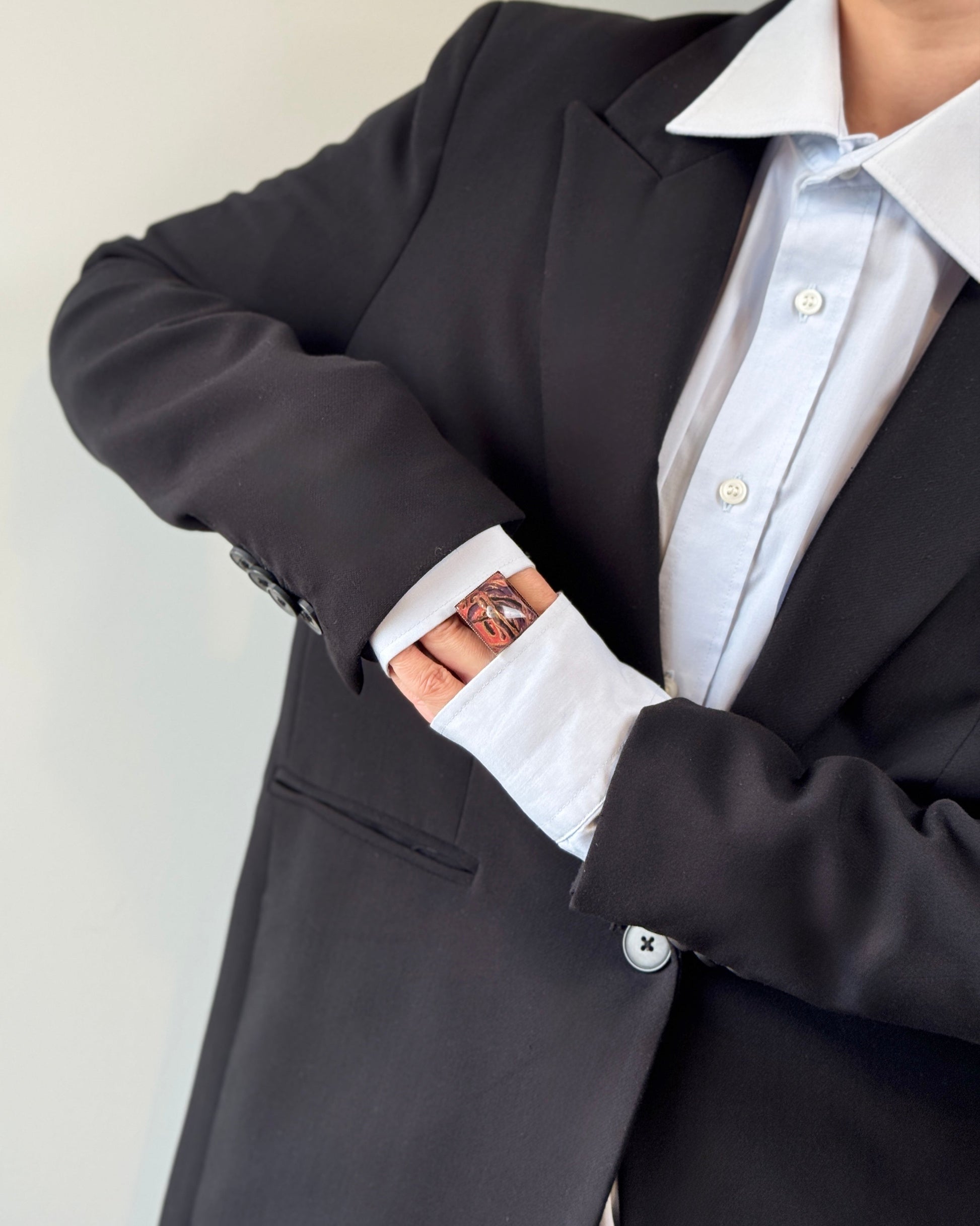 Person wearing a black blazer over a white shirt with rolled-up sleeves against a neutral background