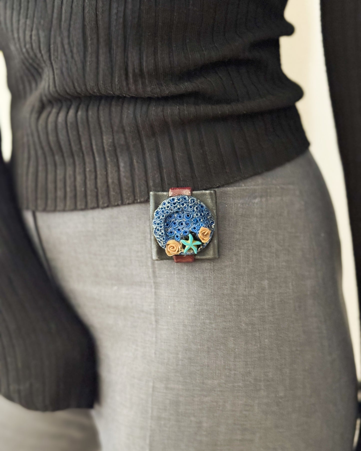 Person wearing a dark sweater and gray pants with a decorative belt buckle featuring a blue design.