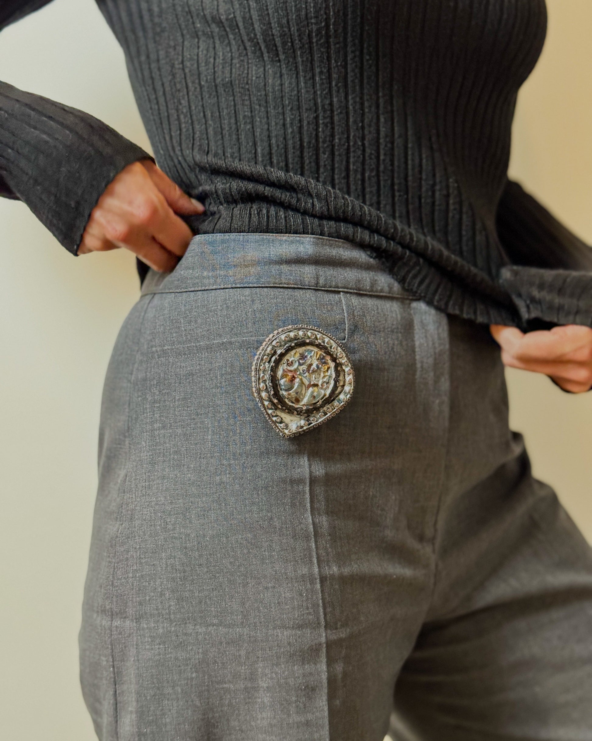 Person wearing a dark ribbed sweater and gray pants with a decorative button on the back pocket.
